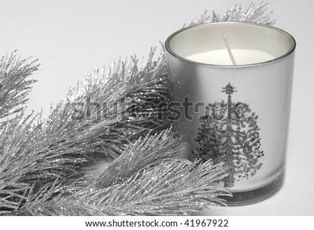 Shining silver fir-tree branch imitation and silver candle in glass with painted xmas-tree on it. On gray background.