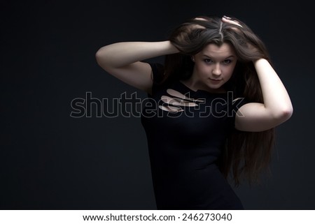 Portrait of teenage girl in black dress with hands in hair on the black background