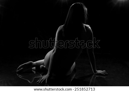Black and white photo of woman sitting back on the floor on black background
