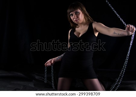 Image of leaned one side plump woman holding chains on black background