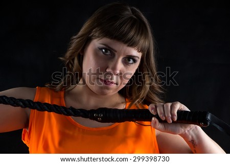Portrait of woman in orange dress with whip on black background