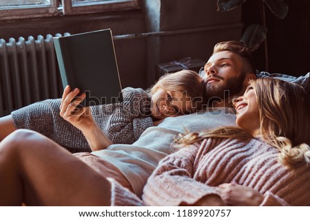 Mom, dad and daughter reading storybook together while lying on bed.