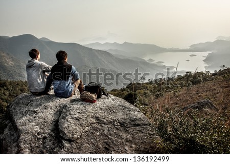 Image of people who are sitting on a big rock while looking far on the landscape