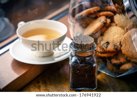 A cup of tea and cookies in a jar by the window