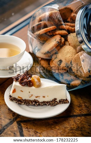 A piece of cheesecake and a cup of tea with a jar of cookies