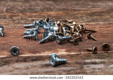 Silver and golden screws scattered on a wooden surface