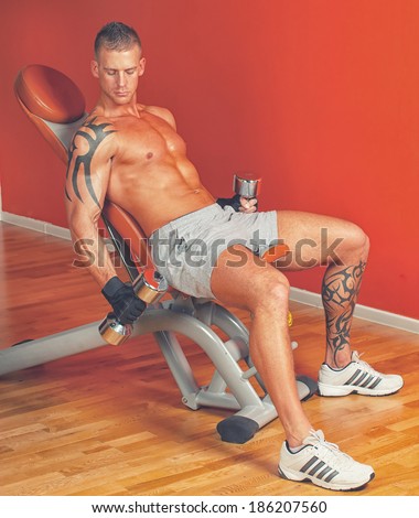 Handsome man with muscles lift a dumbbell on a seat trainer
