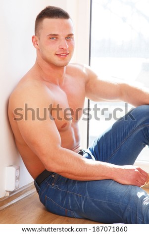 A man with no shirt sitting on the floor