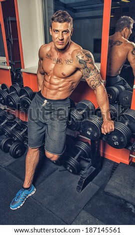 Image of sportsman who leaned on dumbbells while have rest