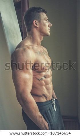 Image of topless man with hands in pockets who is staring in window