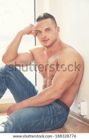 Man wearing no shirt sits on the floor