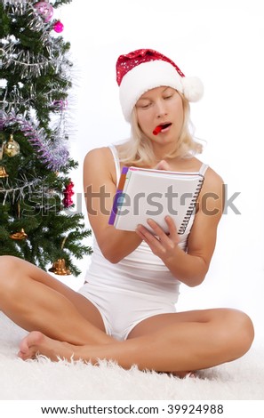 Portrait of sexy girl sitting near christmas tree and writing notes in her diary
