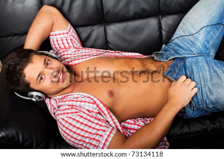 Portrait of a relaxed young guy enjoying music on headphone while lying on sofa at home