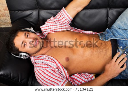 Portrait of a relaxed young guy enjoying music on headphone while lying on sofa at home