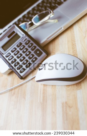 A computer mouse next to a calculator, laptop and glasses