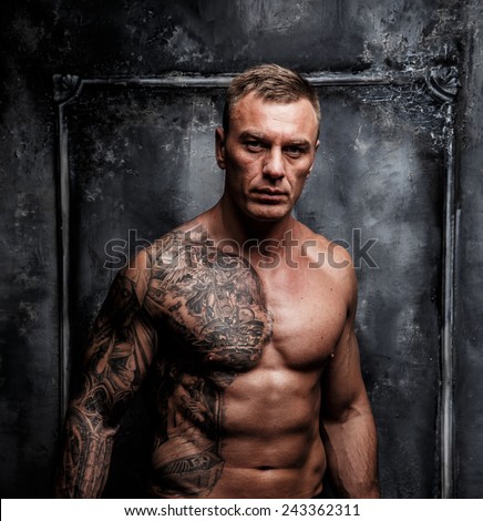 Muscular strong male with tattoo poses over the wall