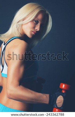 Good-shaped athletic girl poses and holds dumbbell