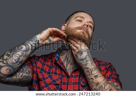 Huge brutal man with tattoo shawing his beard with a razor