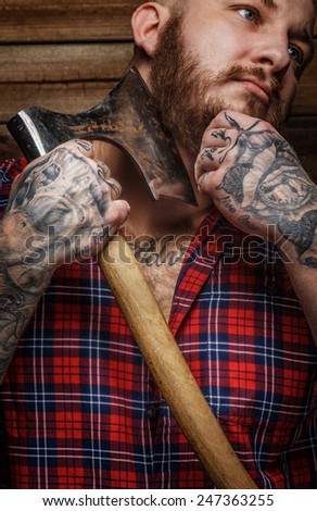 Brutal huge male with tattooes shaves his beard with a big axe