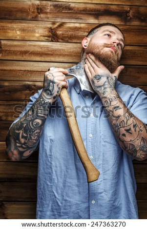 Brutal huge male with tattooes shaves his beard with a big axe