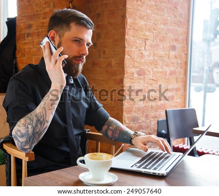 Serious man with tattooes talking on a phone  siiting in coffee shop