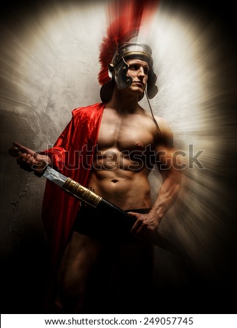 Muscular warrior with sword and helmet posing in front of concrete wall