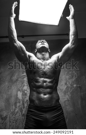 Muscular man with great body relief watching up on white light. Grey background.