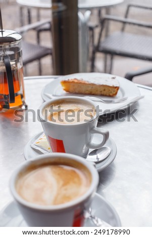 White cups with coffe and white dishes with pieces of cake with nuts on the table.