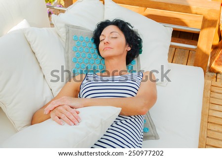 Middle age woman with black hair in a striped dress laying on the beach sofa. Azure rug for massage.