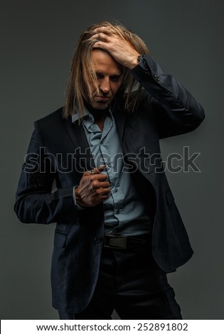 Portrait of handsome middle age long-haired stylish man in dark grey suit. Isolated on gray background.