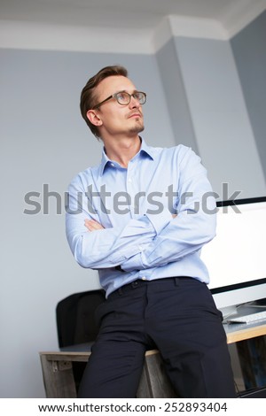 Young business man in office in dark blue suit pants and blue shirt wearing glasses.