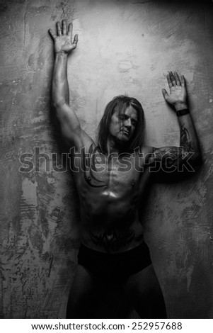 B/W portrait of handsome long-haired man with naked torso. Isolated on gray background. Tattoed male body.