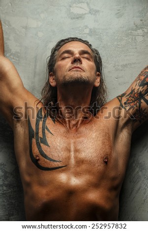 Portrait of handsome long-haired man with naked torso. Isolated on gray background. Tattoed male body.