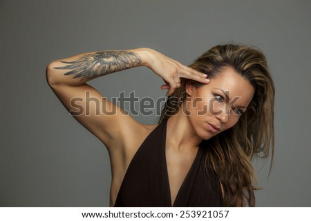 Portrait of long hair woman in long brown dress. Tattoo on hand. Isolated on grey background.