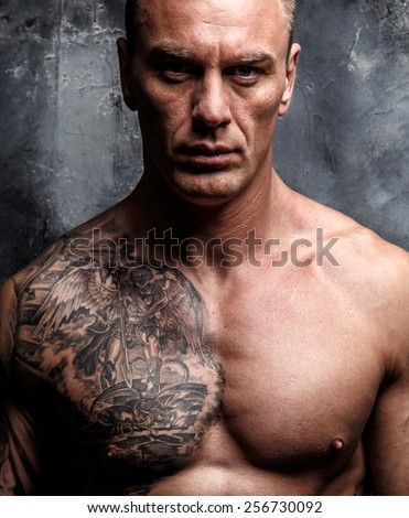 Muscular strong male with tattoo poses over the wall