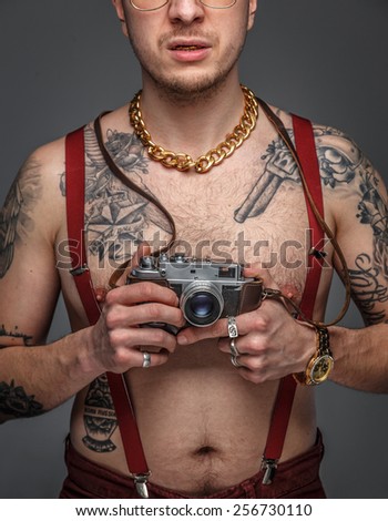 Man with tattoos on his body holding photo camera. Isolated on grey.