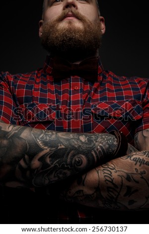 Portrait of male in red shirt and black bow tie with tattoes on his hands. Isolated on dark grey.