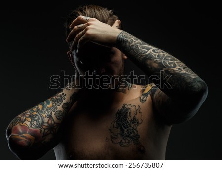 Portrait of a man with naked torso and tattooes. Dark and deep shadows.