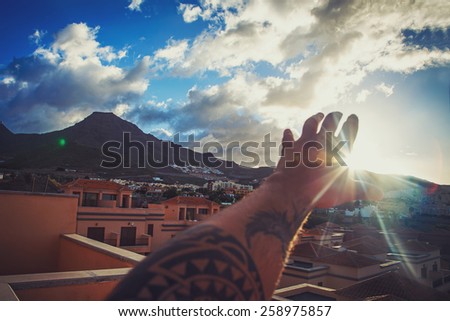 Man\'s hand with tattoo over town and blue sky with fluffy clouds