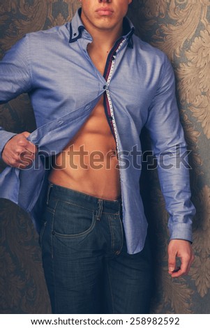 Fashion portrait of man in shirt showing his abs and poses over wall