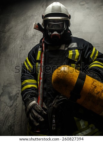 Firefighter in uniform with axe and oxygen on grey background