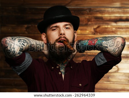 Handsome tattooed man with cigar posing over wood wall