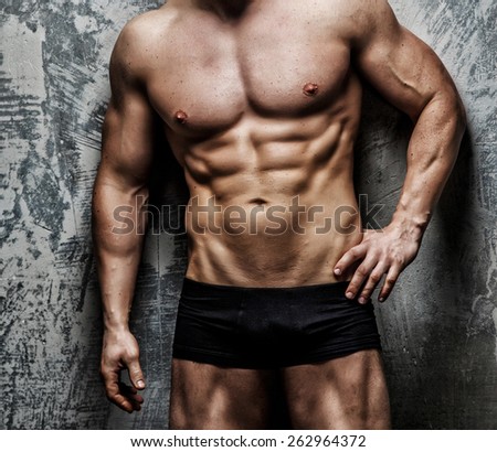 Handsome, muscular, sexy male body in black swimming trunks on gray background.