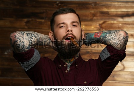 Handsome tattooed man with cigar posing over wood wall