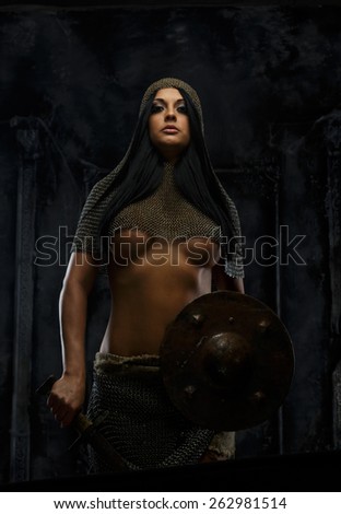 Young female with sword and shield in ancient armor on grey background
