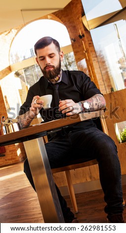 male with tattoos sitting at the table in a cafe.