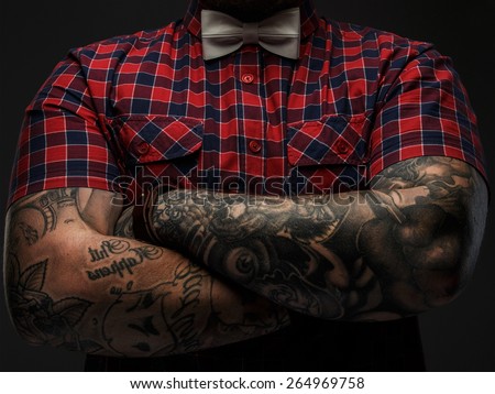 Portraite of brutal hipster with tattooes on his hand dressed in red shirt and bow tie.