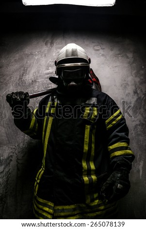 Firefighter in oxygen mask and axe on grey background.