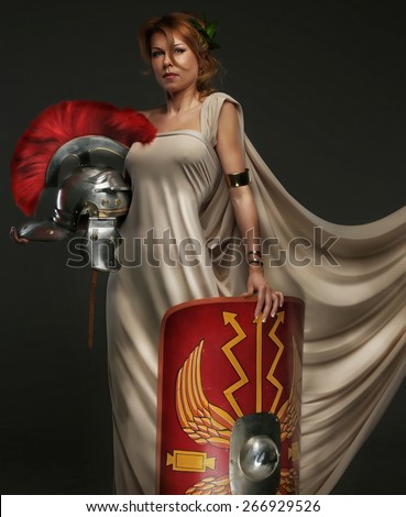 Beautiful woman in roman clothing with shield and helmet. Isolated on grey