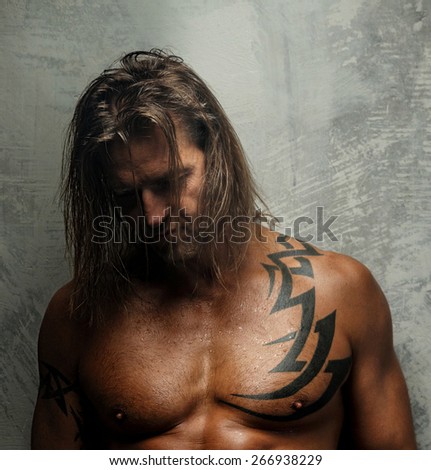 Portrait of handsome long-haired man with naked torso. Isolated on gray background. Tattoed male body.